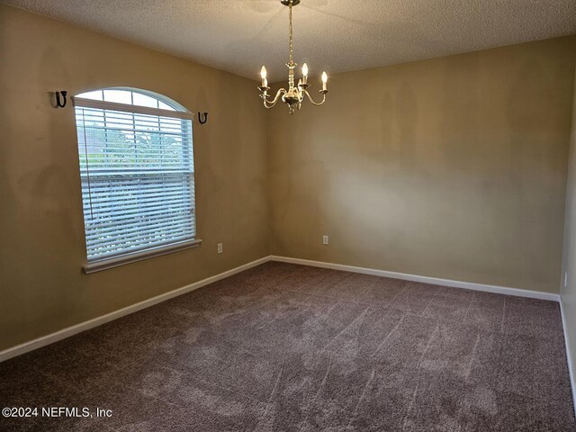 unfurnished room with a notable chandelier, a textured ceiling, and carpet