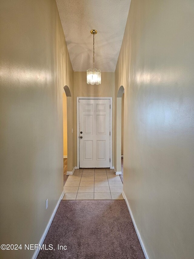 doorway to outside with a chandelier, a textured ceiling, and light tile flooring