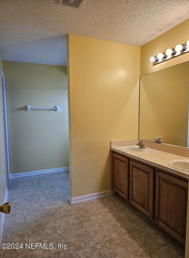 bathroom featuring a textured ceiling, a sink, visible vents, baseboards, and double vanity