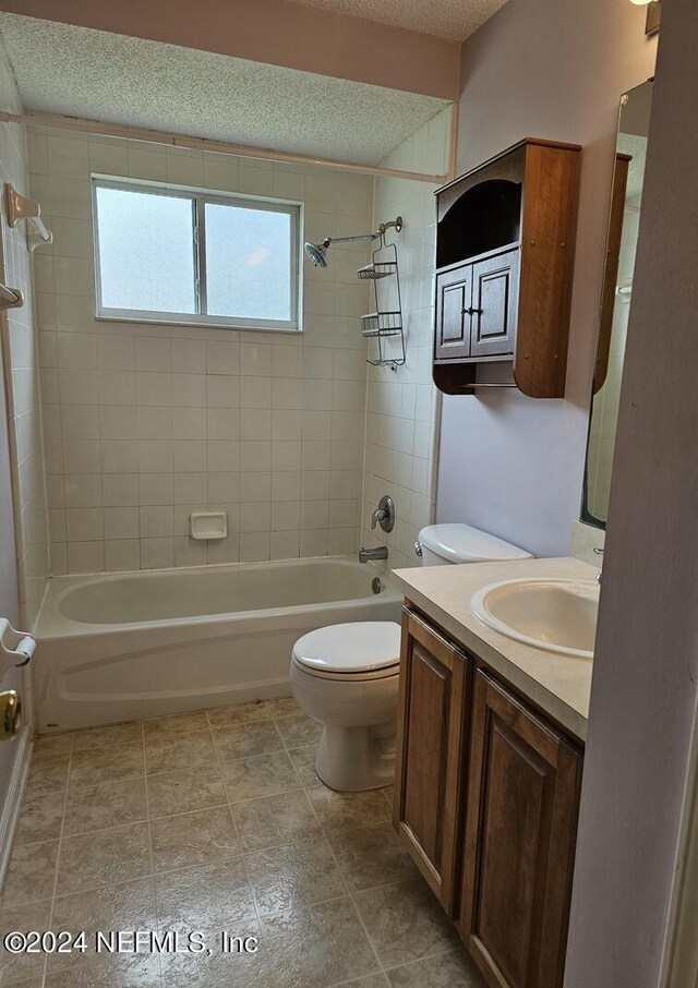 full bathroom featuring a textured ceiling, tiled shower / bath, tile floors, vanity, and toilet