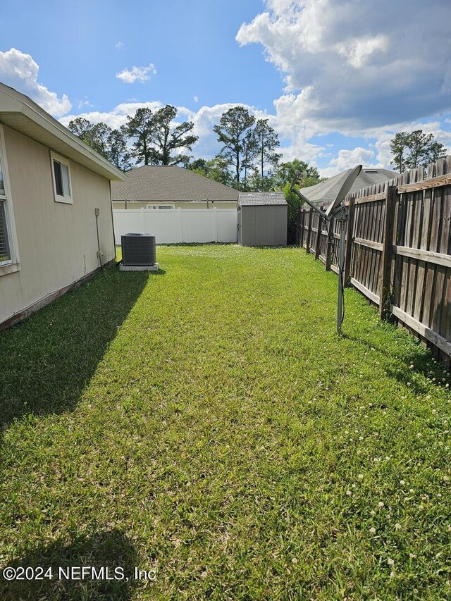 view of yard featuring a storage shed, an outbuilding, a fenced backyard, and central air condition unit