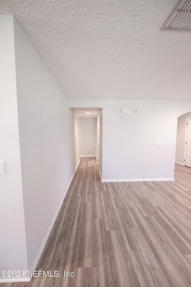 unfurnished room featuring visible vents, a textured ceiling, baseboards, and wood finished floors