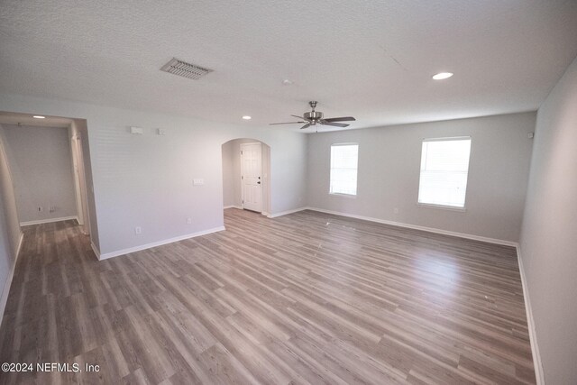 empty room featuring arched walkways, wood finished floors, visible vents, and baseboards