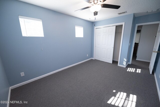 unfurnished bedroom with baseboards, visible vents, dark carpet, and a closet