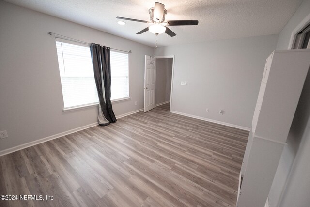 unfurnished bedroom with a ceiling fan, a textured ceiling, baseboards, and wood finished floors