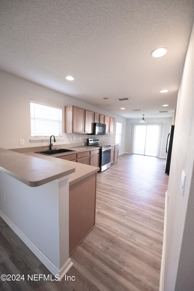 kitchen with freestanding refrigerator, a sink, light wood-type flooring, black microwave, and stainless steel electric range