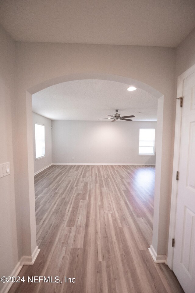 spare room with light wood-style floors, baseboards, arched walkways, and ceiling fan