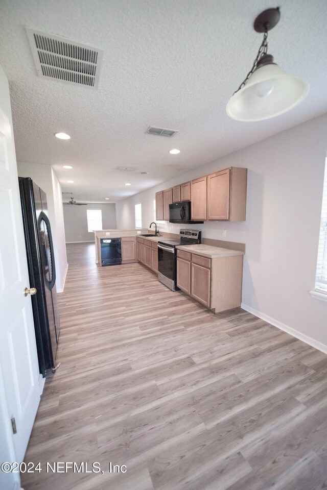 kitchen featuring visible vents, light wood-style flooring, a sink, a peninsula, and black appliances