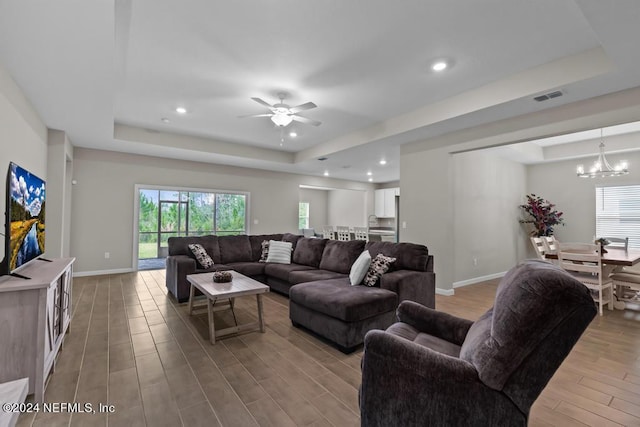 living room with ceiling fan with notable chandelier and a raised ceiling