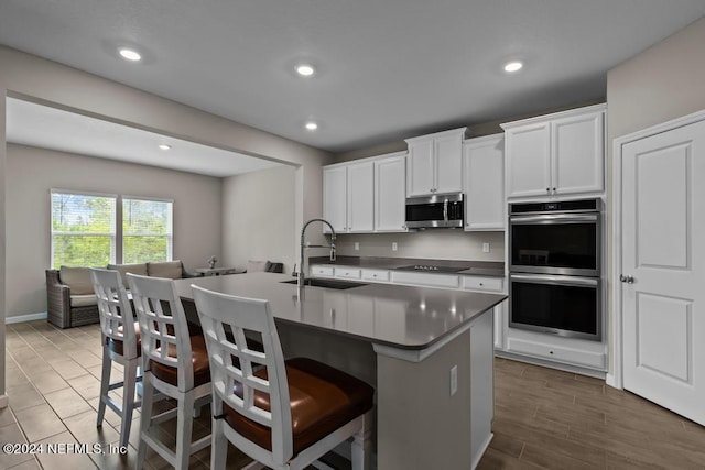 kitchen with a kitchen breakfast bar, stainless steel appliances, a kitchen island with sink, sink, and white cabinets