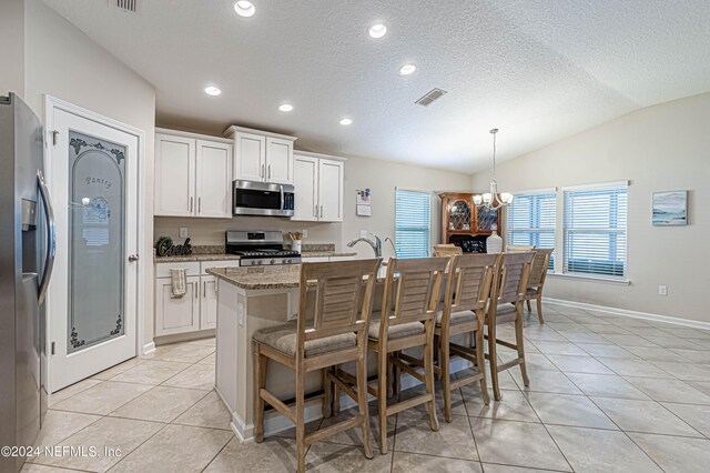 kitchen featuring a center island with sink, white cabinets, hanging light fixtures, vaulted ceiling, and stainless steel appliances