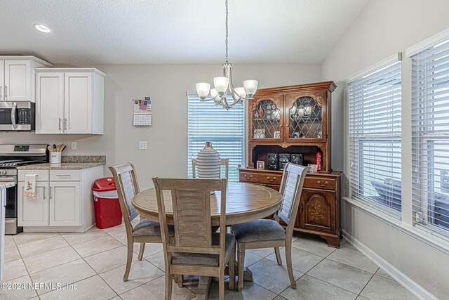 dining room featuring a healthy amount of sunlight, vaulted ceiling, a notable chandelier, and light tile patterned flooring