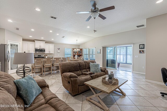 living room featuring lofted ceiling, ceiling fan with notable chandelier, a textured ceiling, a wealth of natural light, and light tile patterned flooring