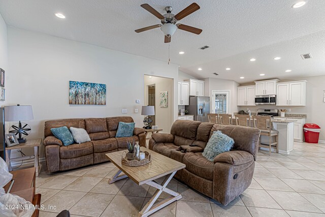 tiled living room with vaulted ceiling, ceiling fan, and a textured ceiling