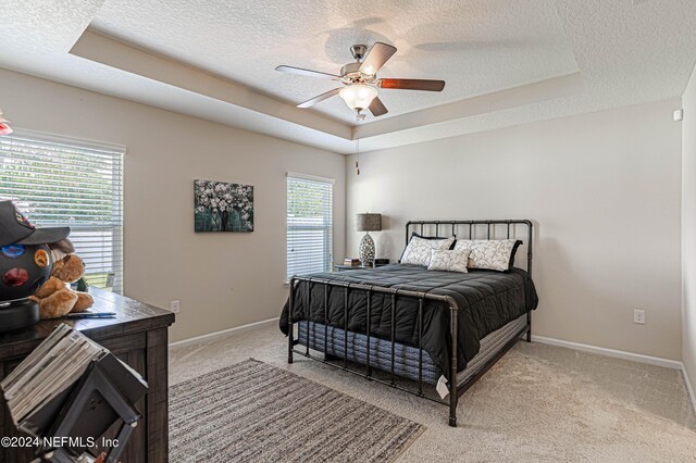 carpeted bedroom with multiple windows, a textured ceiling, a raised ceiling, and ceiling fan