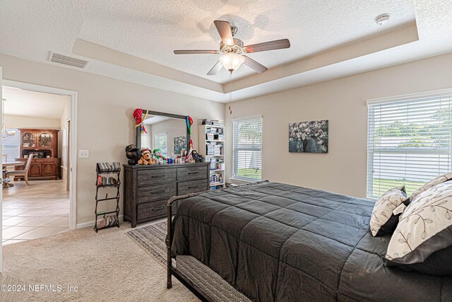 bedroom featuring a tray ceiling, ceiling fan, light colored carpet, and a textured ceiling