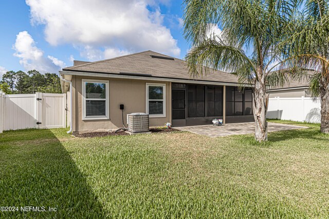 rear view of property with a sunroom, a patio area, central air condition unit, and a yard