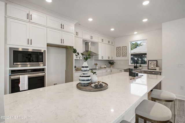 kitchen with light stone countertops, appliances with stainless steel finishes, white cabinetry, and wall chimney exhaust hood