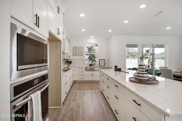 kitchen with light wood-type flooring, stainless steel appliances, sink, a center island, and white cabinetry