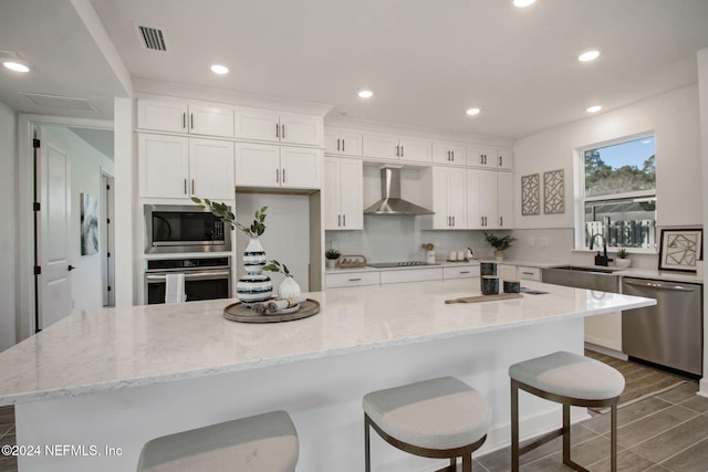 kitchen featuring white cabinetry, sink, wall chimney exhaust hood, stainless steel appliances, and a kitchen island