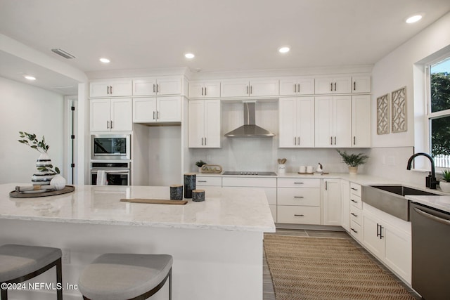 kitchen featuring white cabinets, wall chimney range hood, sink, appliances with stainless steel finishes, and light stone counters