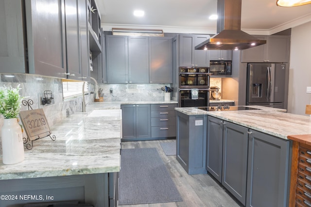 kitchen featuring decorative backsplash, island exhaust hood, light stone counters, black appliances, and crown molding