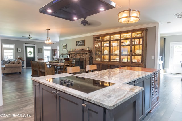 kitchen with hanging light fixtures, black electric cooktop, ceiling fan, a fireplace, and light stone countertops