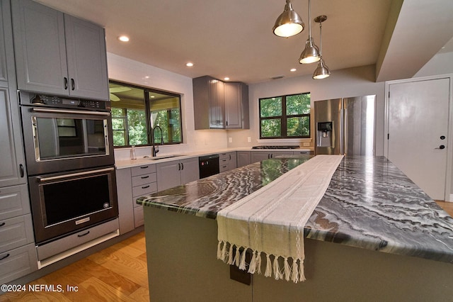 kitchen with sink, appliances with stainless steel finishes, gray cabinets, pendant lighting, and light hardwood / wood-style floors