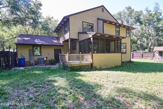 rear view of house featuring cooling unit, a sunroom, a wooden deck, and a lawn