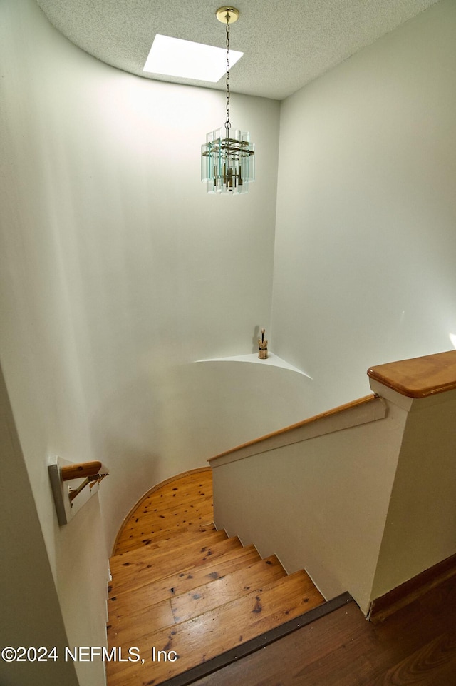 staircase with hardwood / wood-style floors, a textured ceiling, a skylight, and a chandelier