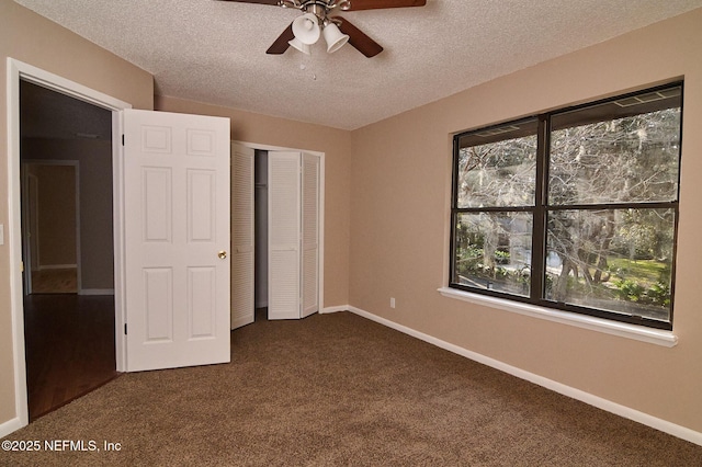 unfurnished bedroom featuring multiple windows, a textured ceiling, ceiling fan, and dark colored carpet