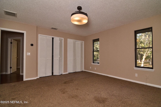 unfurnished bedroom with multiple closets, dark carpet, multiple windows, and a textured ceiling