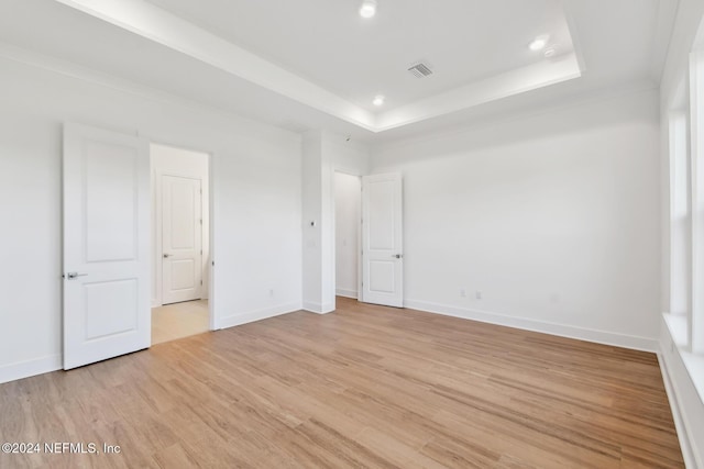 unfurnished bedroom featuring light wood-type flooring and a tray ceiling