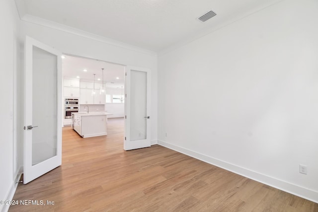 empty room with sink, ornamental molding, light hardwood / wood-style flooring, and french doors