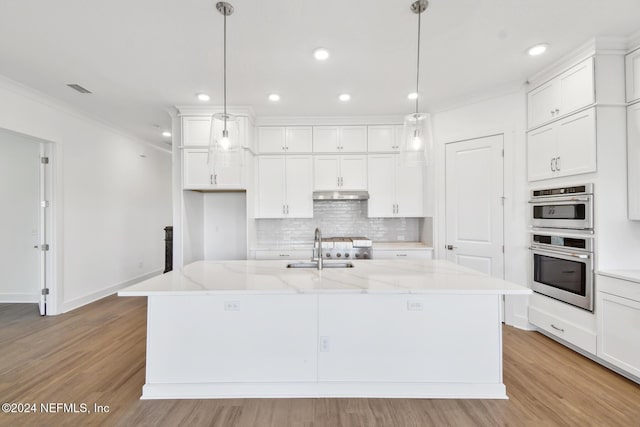 kitchen with white cabinets, decorative light fixtures, a center island with sink, and light stone countertops