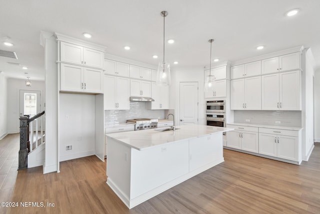 kitchen with light hardwood / wood-style floors, white cabinetry, sink, and an island with sink