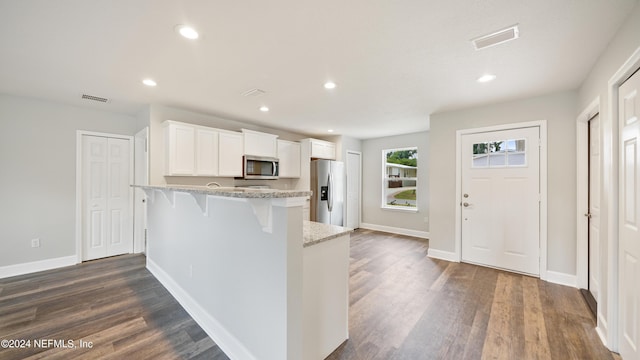 kitchen featuring light stone countertops, appliances with stainless steel finishes, a breakfast bar, dark wood-type flooring, and white cabinetry