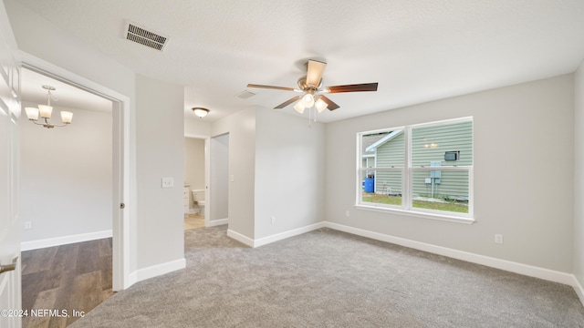 empty room featuring ceiling fan with notable chandelier, carpet floors, and a textured ceiling