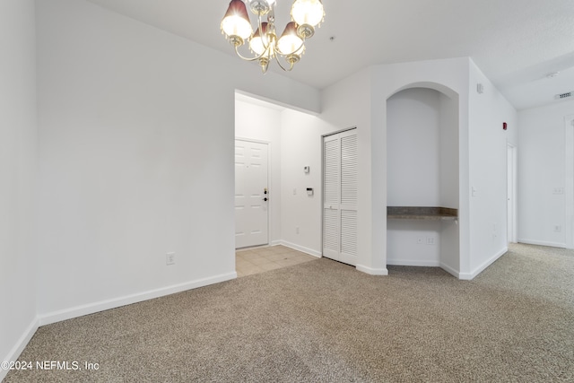 spare room featuring light carpet and a chandelier