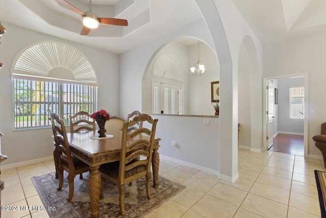 tiled dining area with ceiling fan with notable chandelier and a tray ceiling