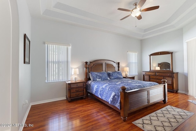 bedroom with a raised ceiling, ceiling fan, and dark wood-type flooring