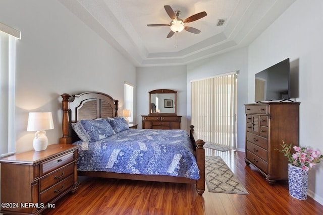 bedroom with dark hardwood / wood-style floors, ceiling fan, and a raised ceiling