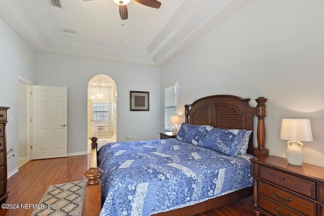 bedroom with ceiling fan, a raised ceiling, wood-type flooring, and ensuite bathroom