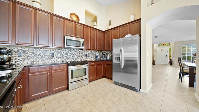 kitchen featuring a high ceiling, stainless steel appliances, backsplash, and light tile floors