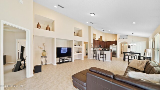 tiled living room featuring built in features, high vaulted ceiling, and a chandelier