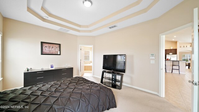 bedroom with a raised ceiling, stainless steel fridge, carpet flooring, and ensuite bathroom