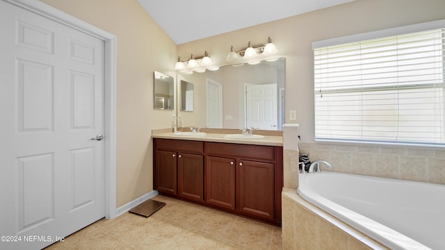 bathroom with dual sinks, tile flooring, vanity with extensive cabinet space, tiled tub, and vaulted ceiling