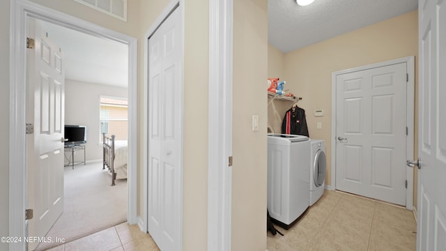 clothes washing area with washer and dryer, a textured ceiling, and light colored carpet