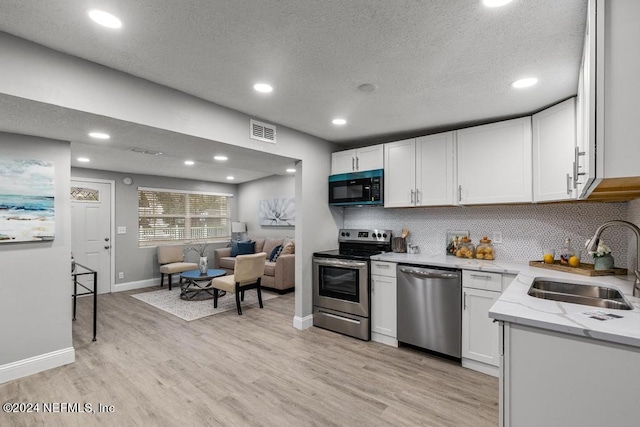 kitchen with a textured ceiling, stainless steel appliances, sink, light hardwood / wood-style flooring, and white cabinetry