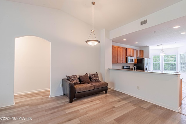 kitchen featuring pendant lighting, lofted ceiling, stainless steel appliances, kitchen peninsula, and light hardwood / wood-style flooring